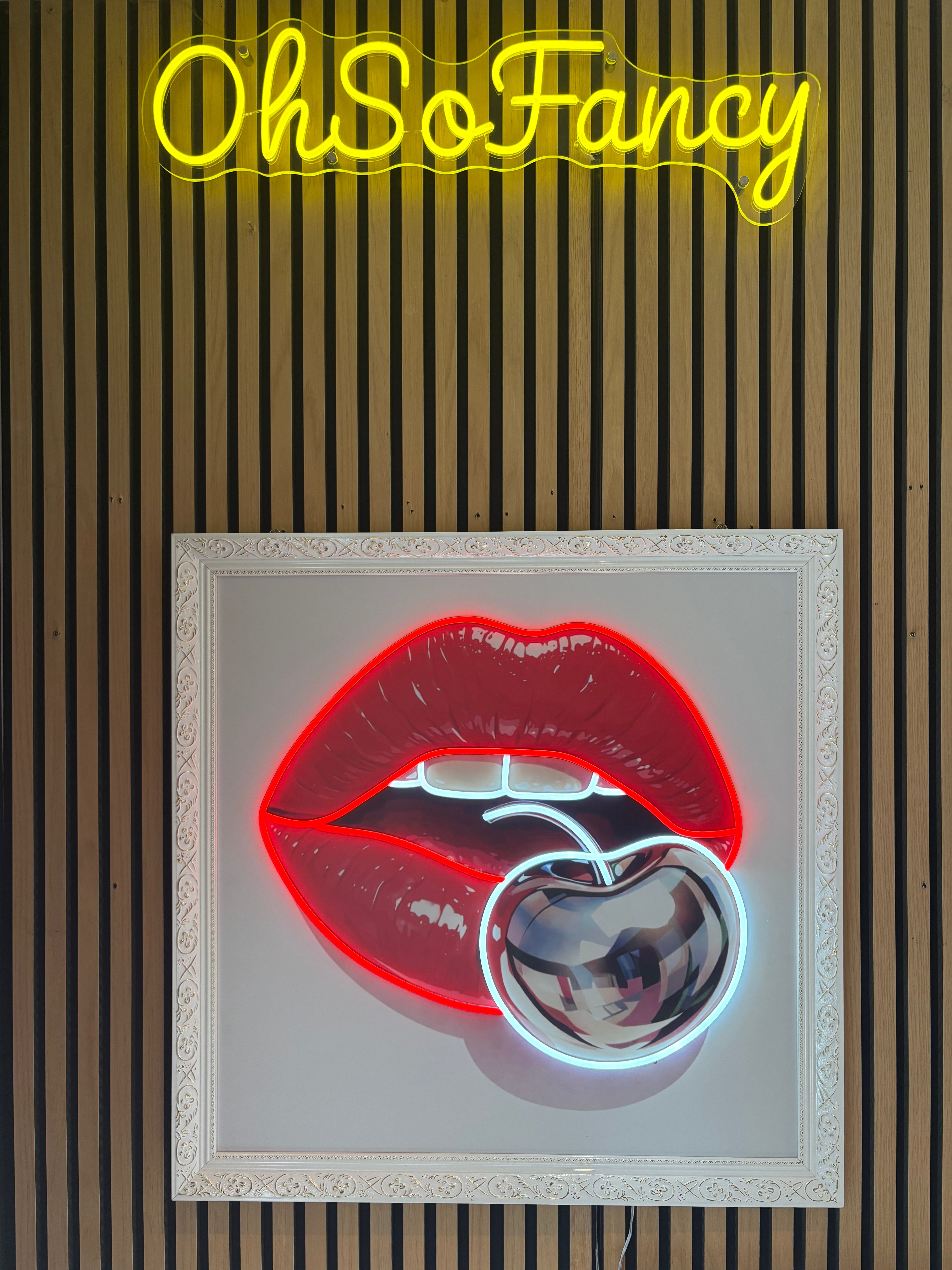 Neon sign with red lips with cherry on a white background, featuring the brand 'OhSoFancy'