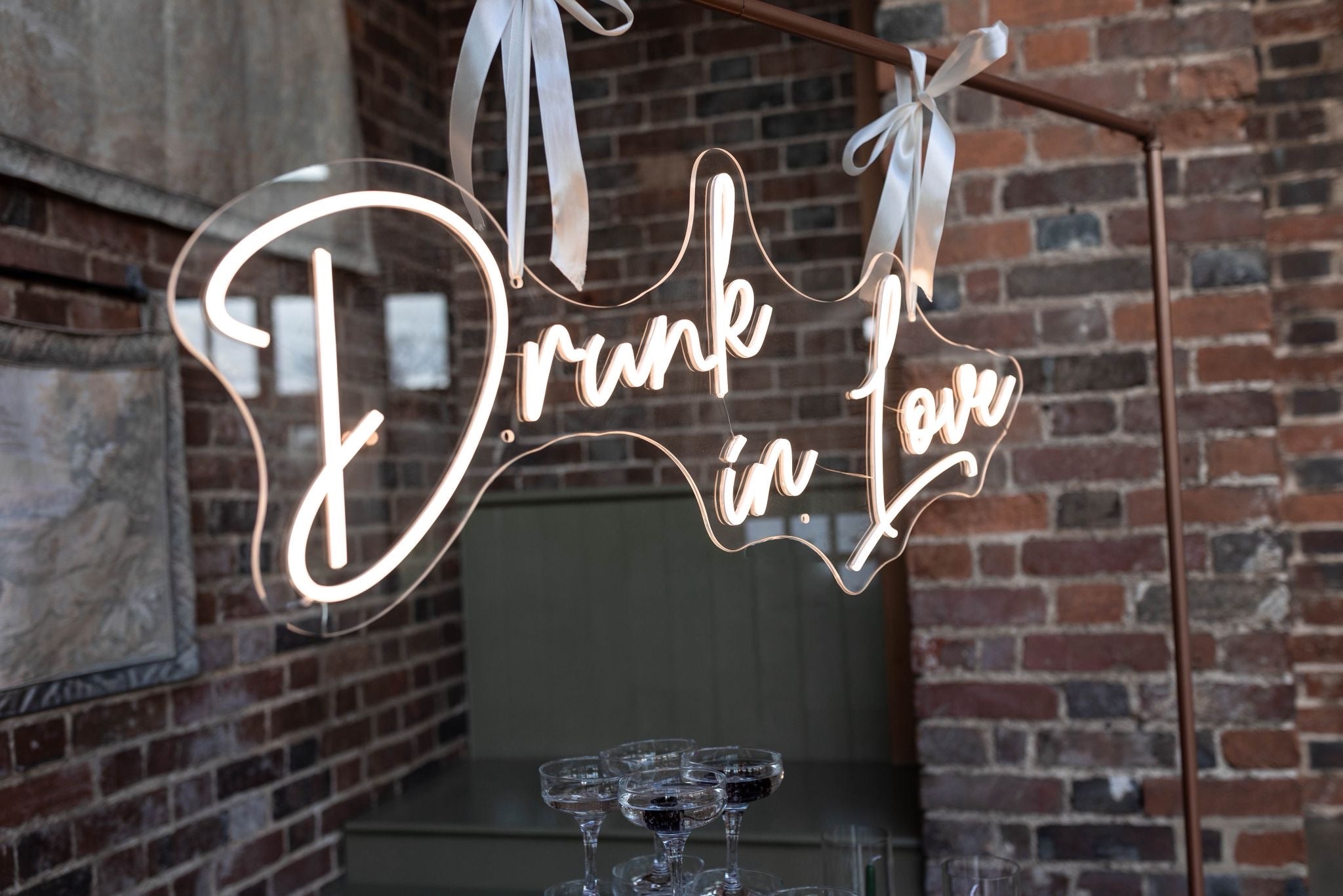 Neon LED sign 'Drunk in Love' text, hanging against a brick wall in a wedding setting.